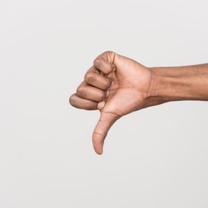 A hand gives a thumbs-down gesture against a plain, light gray background.