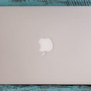 Closed silver laptop resting on a weathered blue wooden surface, displaying a partially bitten apple logo in the center.