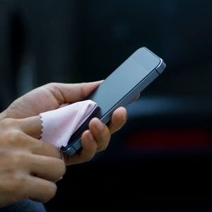 A smartphone is being wiped with a soft cloth, held in one hand against a dark background.