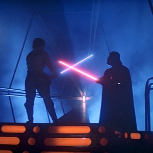 Two figures clash with glowing swords, silhouetted against a smoky, blue-lit futuristic setting.