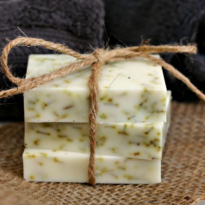 Three bars of speckled soap tied with twine, resting on burlap fabric with dark towels in the background.