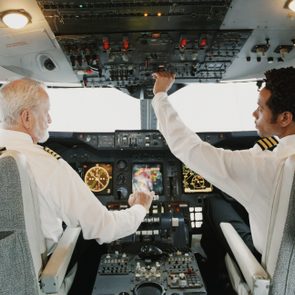 Pilots operate controls in a plane cockpit, surrounded by instruments, gauges, and switches.