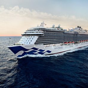 Cruise ship sails on open ocean under a clear sky, displaying 