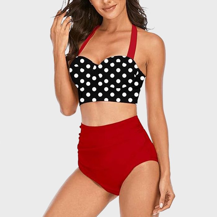 Woman wears a black polka-dot top with red straps, paired with high-waisted red bottoms, standing against a plain light background.
