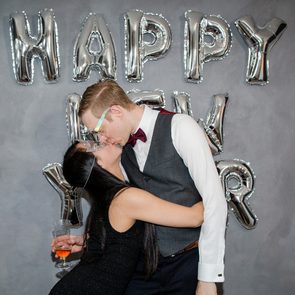 Two people kiss in front of silver balloon letters spelling 