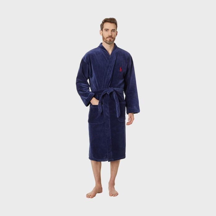 A person wears a blue robe with a red emblem, standing barefoot against a plain gray background.