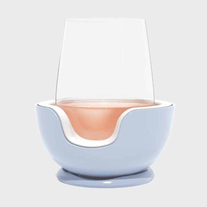 A transparent glass holds a pink liquid, resting on a smooth, blue ceramic base with a cut-out design, against a plain background.